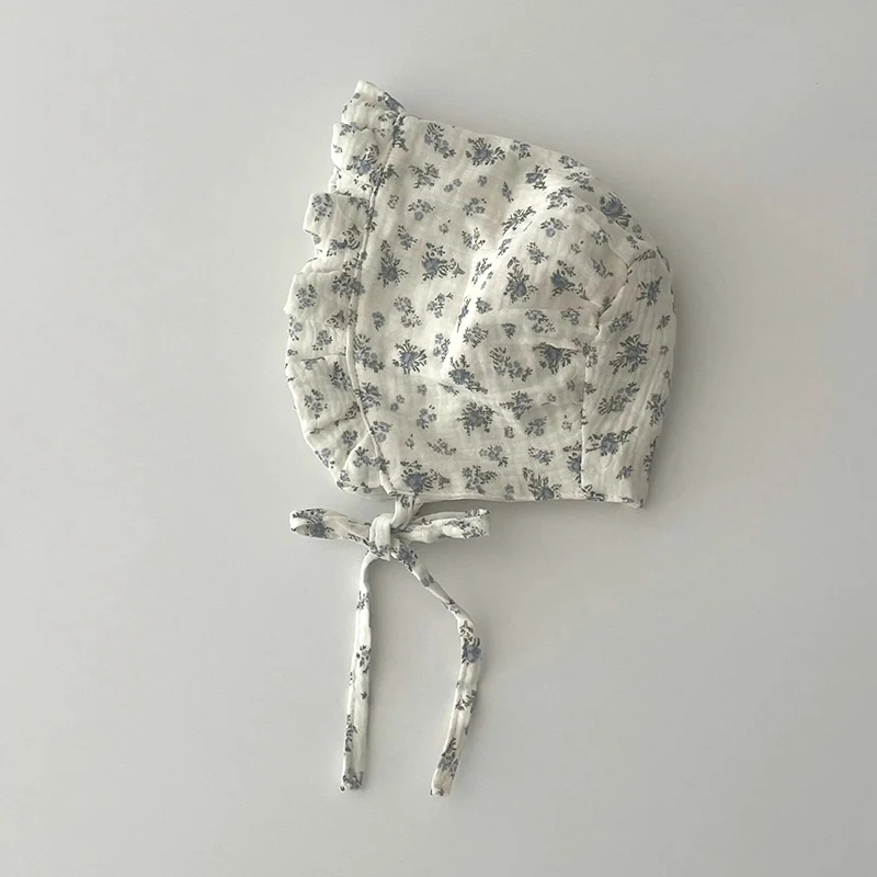 Bébé dans une robe blanche et un chapeau floral, assis dans l'herbe